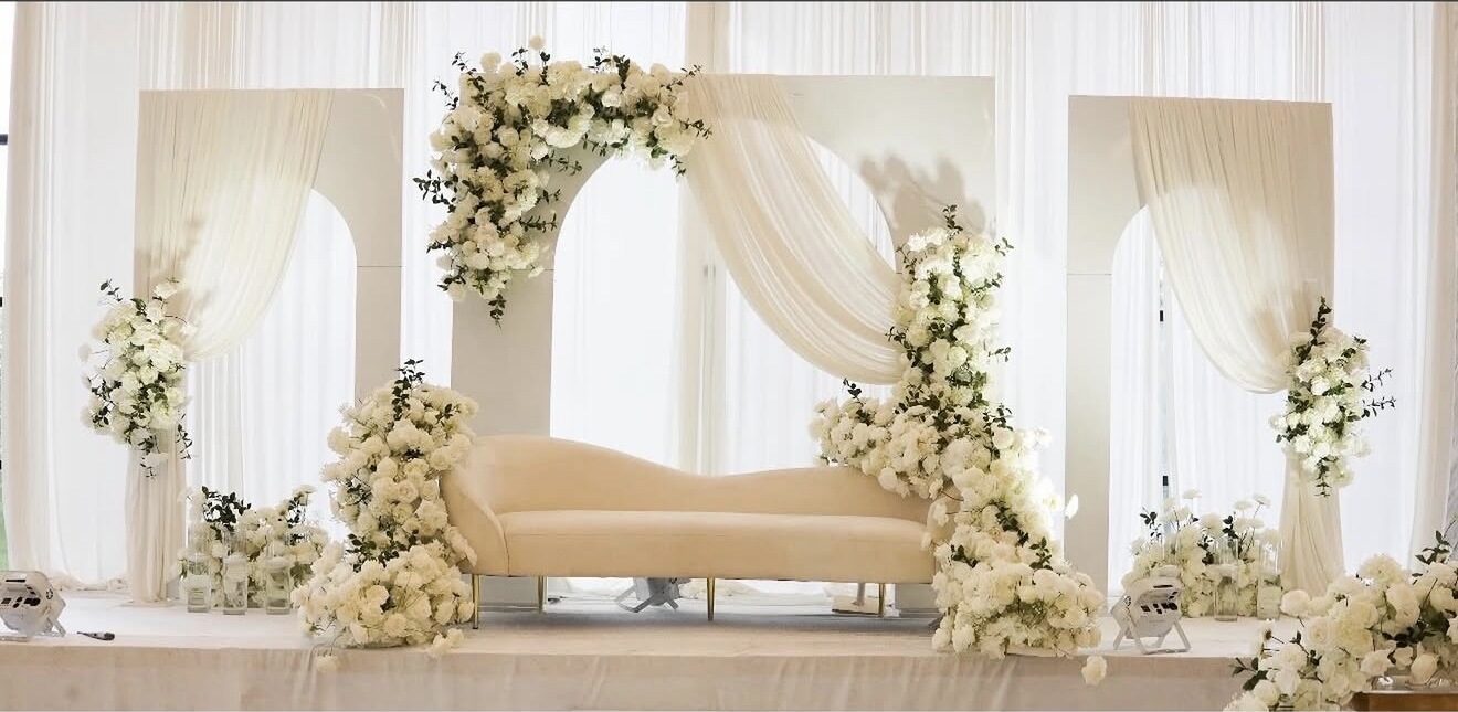 Ivory triple-arch stage with cascading white florals and a cream sofa