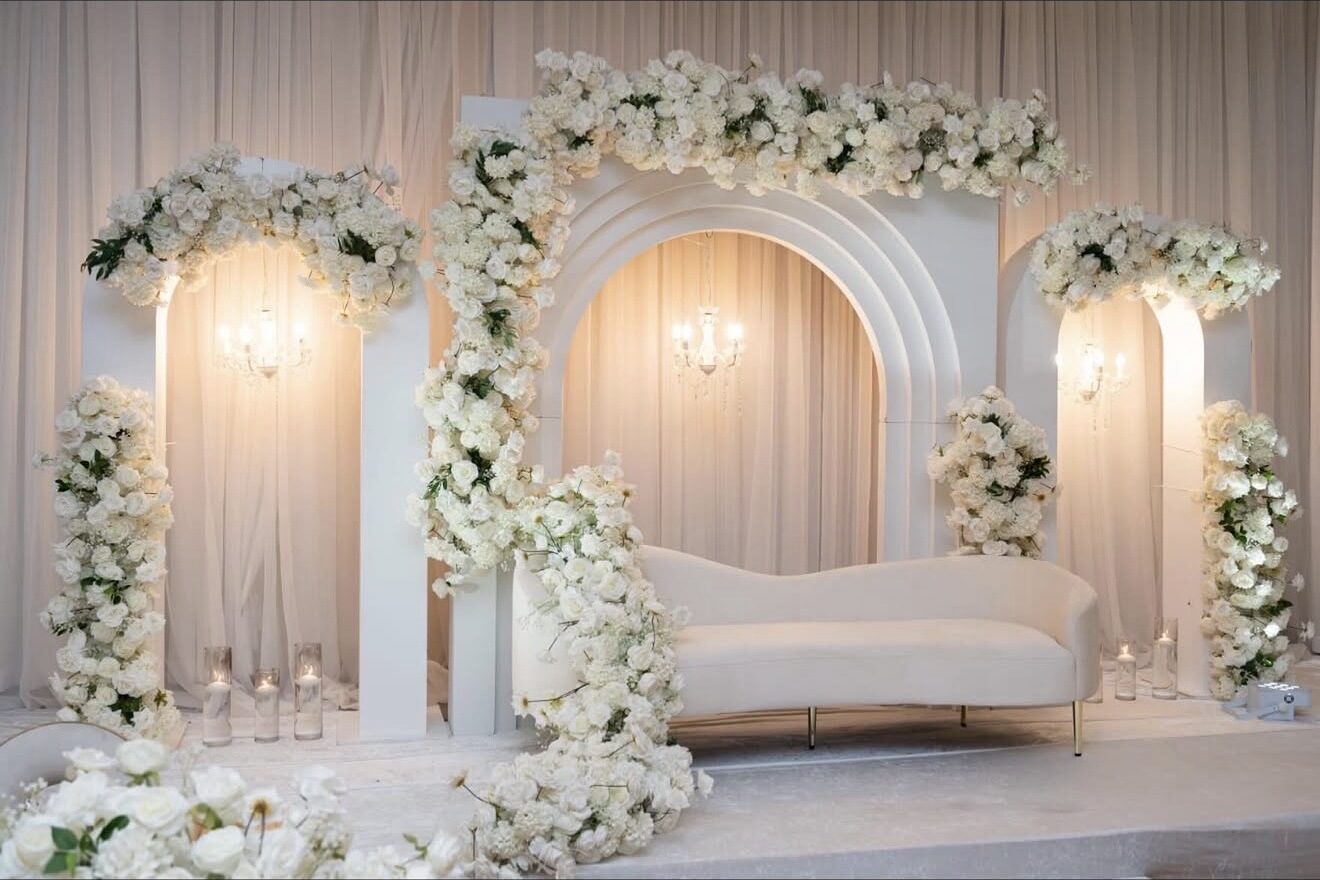Warm-lit white floral triple-arch stage with a cream sofa
